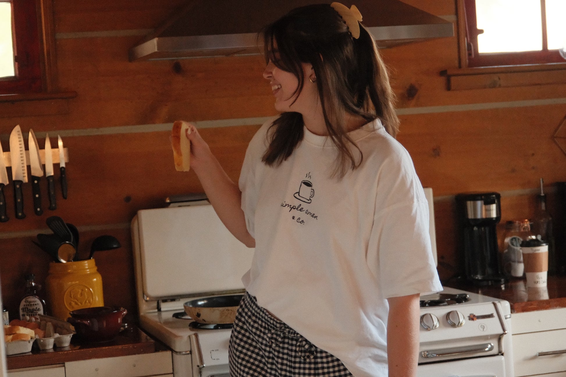 Person holding a piece of bread with blueberries, wearing a white t-shirt with a coffee cup design and text saying "simple amen & co"